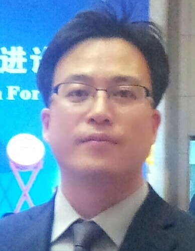 A man in a suit is standing in front of a blue background with a circular emblem. (Captioned by AI)
