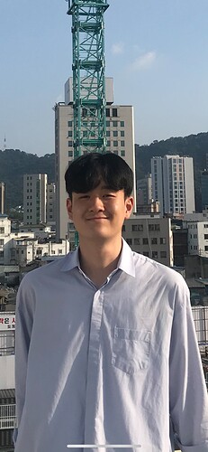 A cheerful young person smiles in front of a cityscape, with buildings and a crane visible in the background. (Captioned by AI)